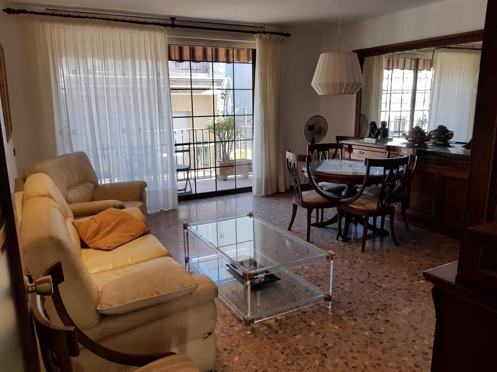 Una sala de estar con un sofá, una mesa de centro de vidrio, un comedor con sillas y una cocina con mesa y sillas.