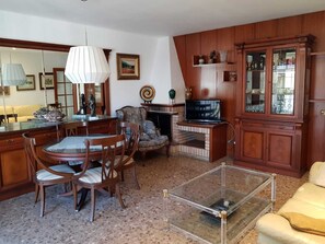 Una sala de estar con un mueble de madera, un televisor, una chimenea y una zona de comedor con sillas y una mesa.