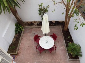A patio with a round table and four chairs, an umbrella, and a small tree.
