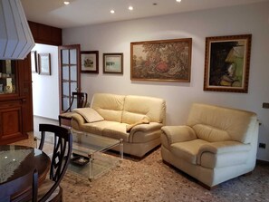 A living room with two beige sofas, a glass coffee table, and a dining table with chairs. There are framed pictures on the wall and a cabinet with glass doors. - A luxury apartment in the center of Calafell (Calafell)