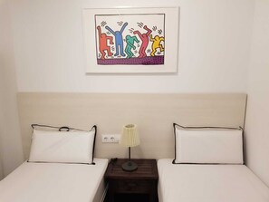 A hotel room with two beds, a nightstand with a lamp, and a framed artwork on the wall.