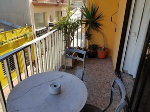 A balcony with a round table and chairs, potted plants, and a yellow building in the background. - A luxury apartment in the center of Calafell (Calafell)