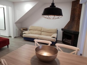 Un salon moderne avec un canapé, une table sur laquelle se trouve un saladier, un luminaire suspendu et une cheminée.