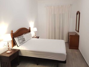 Un lit bien fait, avec une tête de lit en bois, deux lampes de chevet, une table de chevet en bois, un miroir au mur et un rideau.