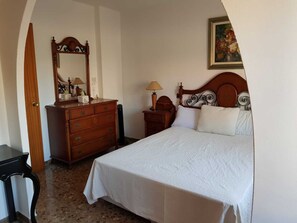 A bedroom with a bed, dresser, nightstand, lamp, and a painting on the wall. - A luxury apartment in the center of Calafell (Calafell)