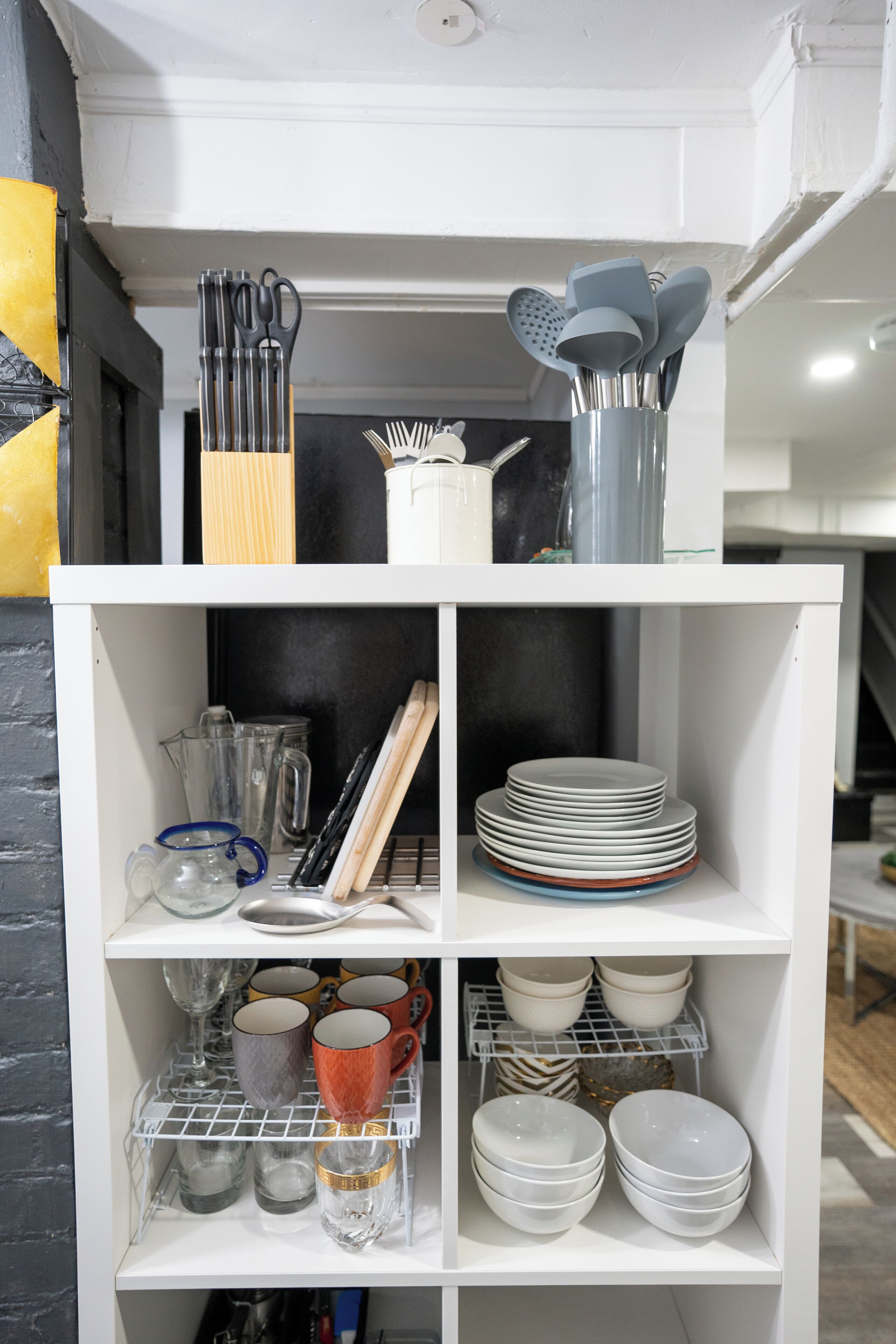 Uma estante branca com utensílios de cozinha, pratos, copos e tigelas.