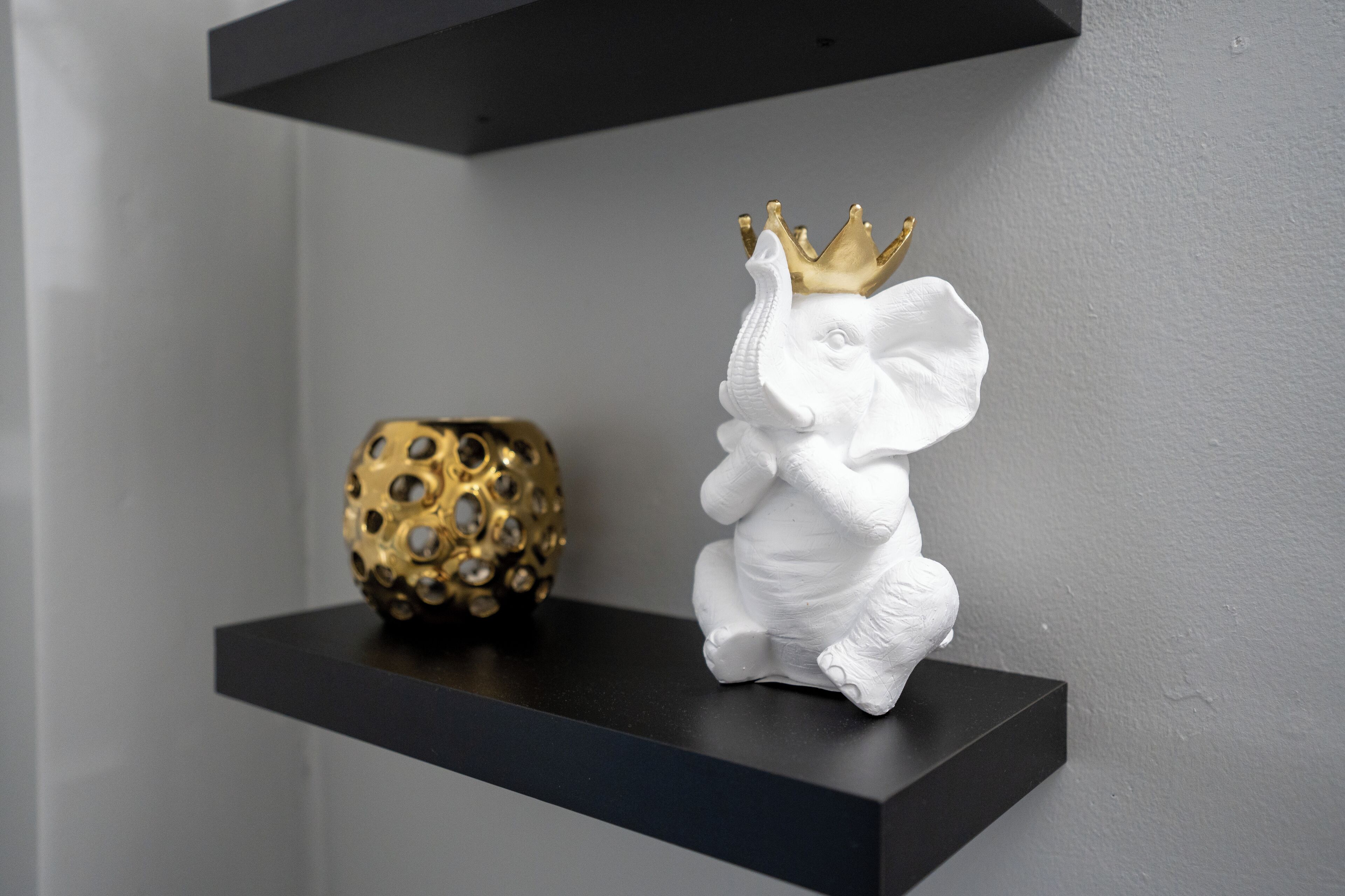 Eine weiße Elefant-Figur mit goldener Krone auf einem schwarzen Regal.