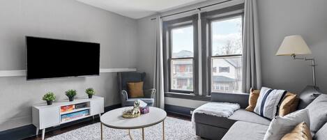 A modern living room with a flat-screen TV, a grey sofa, a coffee table, and a ceiling fan.