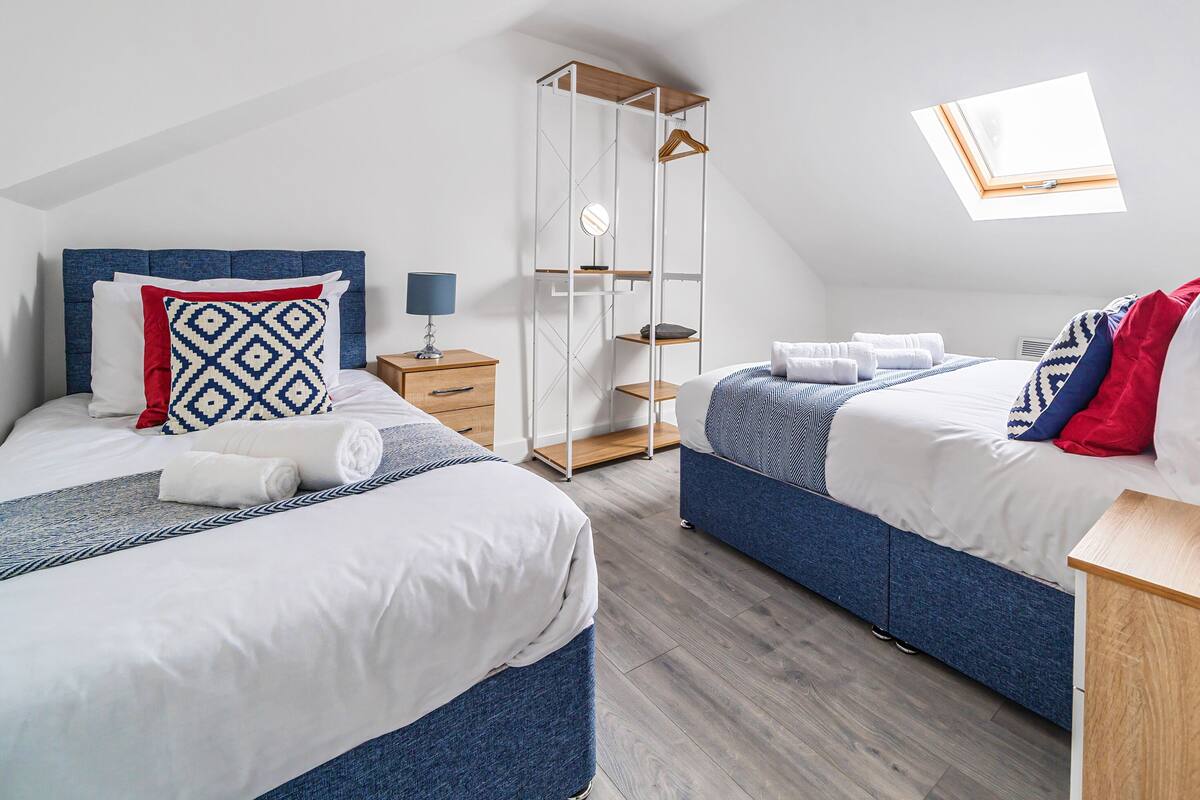 Ein modernes Schlafzimmer mit zwei Betten, einem Oberlicht, einem Kleiderschrank und einem Nachttisch mit Lampe.