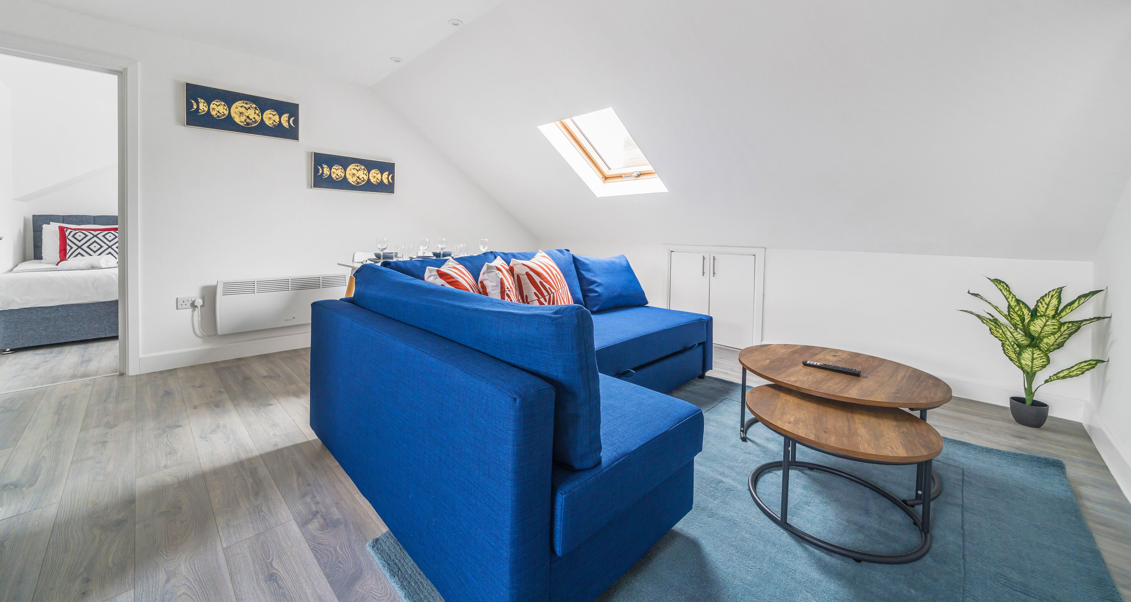 Una sala de estar moderna con un sofá azul, una mesa redonda de madera y un tragaluz.