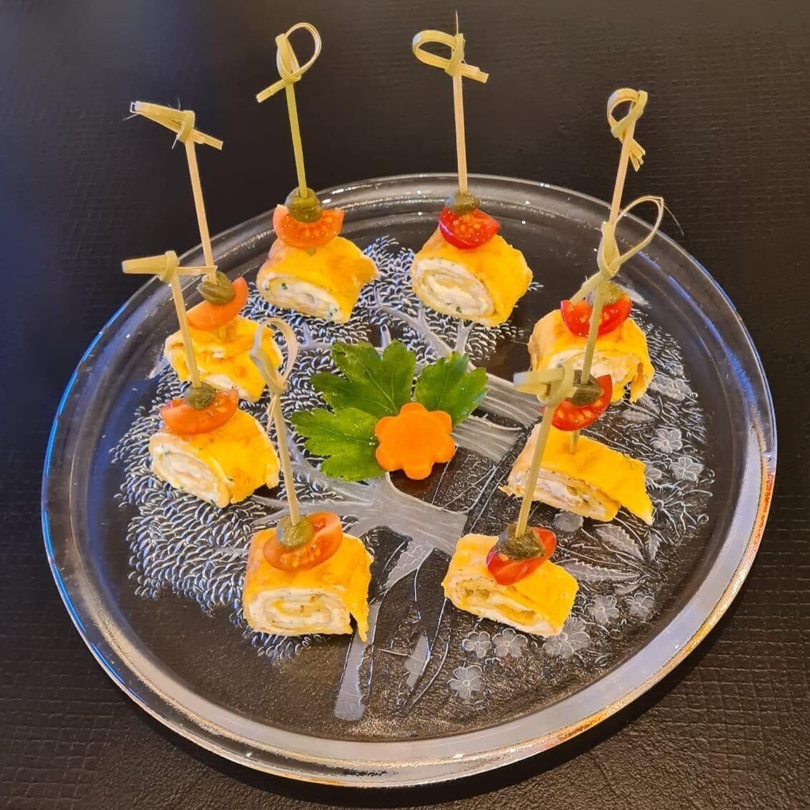 Ein Teller mit Vorspeisen, mit Zahnstochern garniert, verziert mit Cocktailtomaten und einer Zierblume.