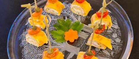A plate of appetizers with toothpicks, garnished with cherry tomatoes and a decorative flower.
