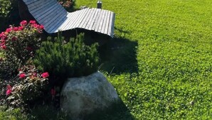 Paisaje rural con una casa de madera rodeada de un césped cuidado y flores de colores.