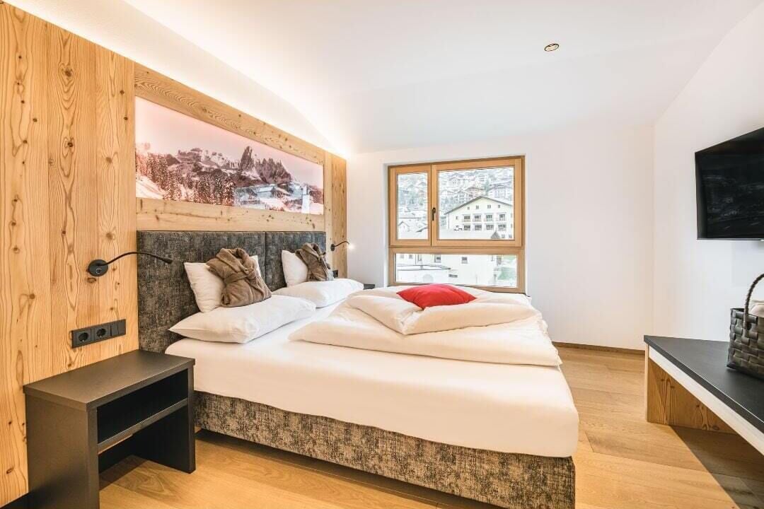 Un dormitorio moderno con una cama, cabecera de madera, televisor y ventana con vista a edificios.