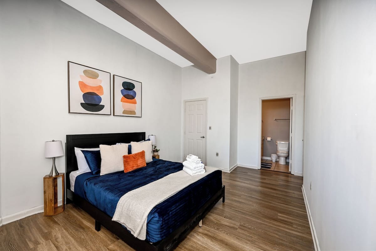 A modern bedroom with a large bed, a nightstand, a lamp, and abstract art on the wall.