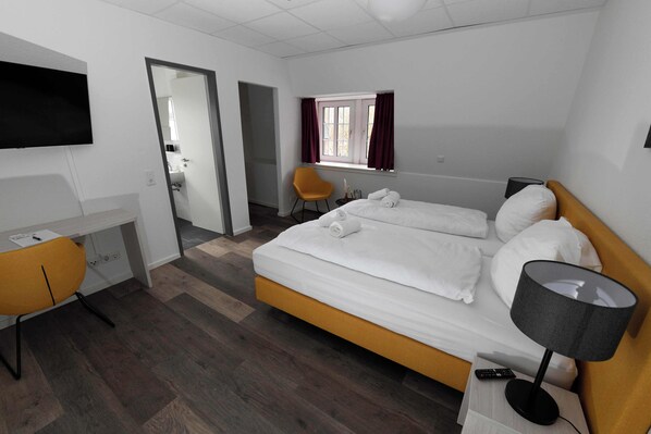 Une chambre d’hôtel avec un lit, un bureau, une chaise, une télévision et une fenêtre avec des rideaux.