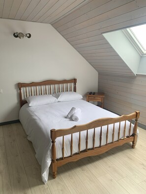 Un dormitorio con techo inclinado, una cama de madera, una mesita de noche con lámpara y un tragaluz.