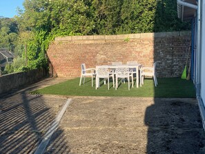 Un patio con pared de ladrillo, una mesa con sillas y una zona de césped.