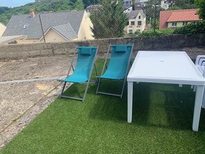 Un patio con dos sillones verdes y una mesa blanca, rodeado por un muro de piedra y una cerca de alambre.