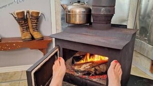 A cozy room with a wood-burning stove, a shelf with boots, and a wall with motivational text. - Skipper's View Cottage by the Sea - Pet Friendly! (Point Leamington)
