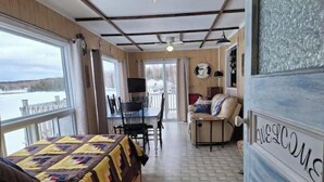 A room with a bed, a desk, and a chair. There is a window with a view of a body of water. - Skipper's View Cottage by the Sea - Pet Friendly! (Point Leamington)