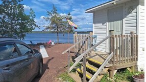 A cabin with a wooden deck, a staircase, and a view of the lake. - Skipper's View Cottage by the Sea - Pet Friendly! (Point Leamington)