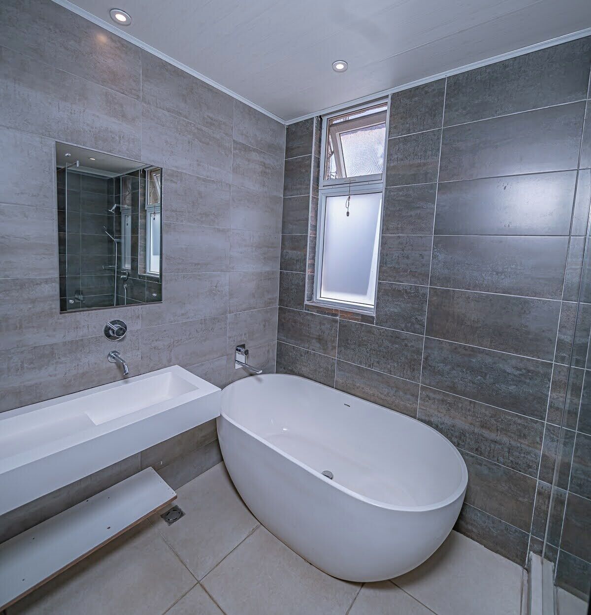 A modern bathroom with a freestanding bathtub, a large mirror, and a window.