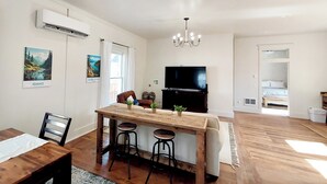 Een moderne woonkamer met een houten eettafel, twee barkrukken, een televisie en een kroonluchter.