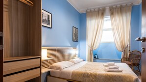 Une chambre à coucher avec un lit, une armoire en bois, une fenêtre avec des rideaux et un tableau accroché au mur.