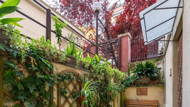 Une petite cour étroite avec un banc en bois, des plantes en pot et un mur en treillis.