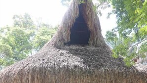 Uma construção com telhado de palha, varanda de madeira, placa com a inscrição "CASADEL PORTAL" e área externa com cadeiras e mesas.
