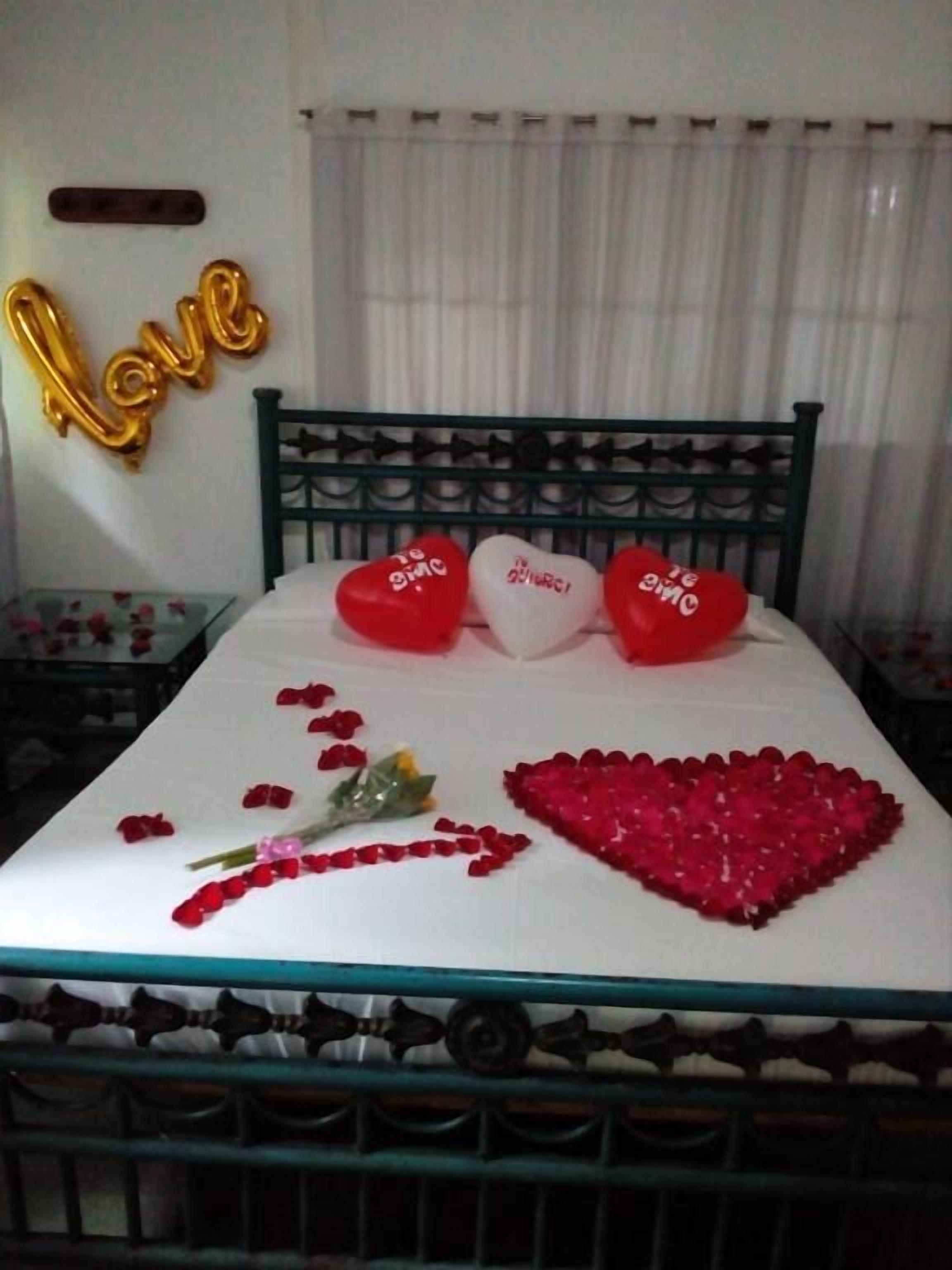 Un lit agrémenté d’oreillers en forme de cœur et d’une décoration faite de pétales de rose sur la couvre-lit.