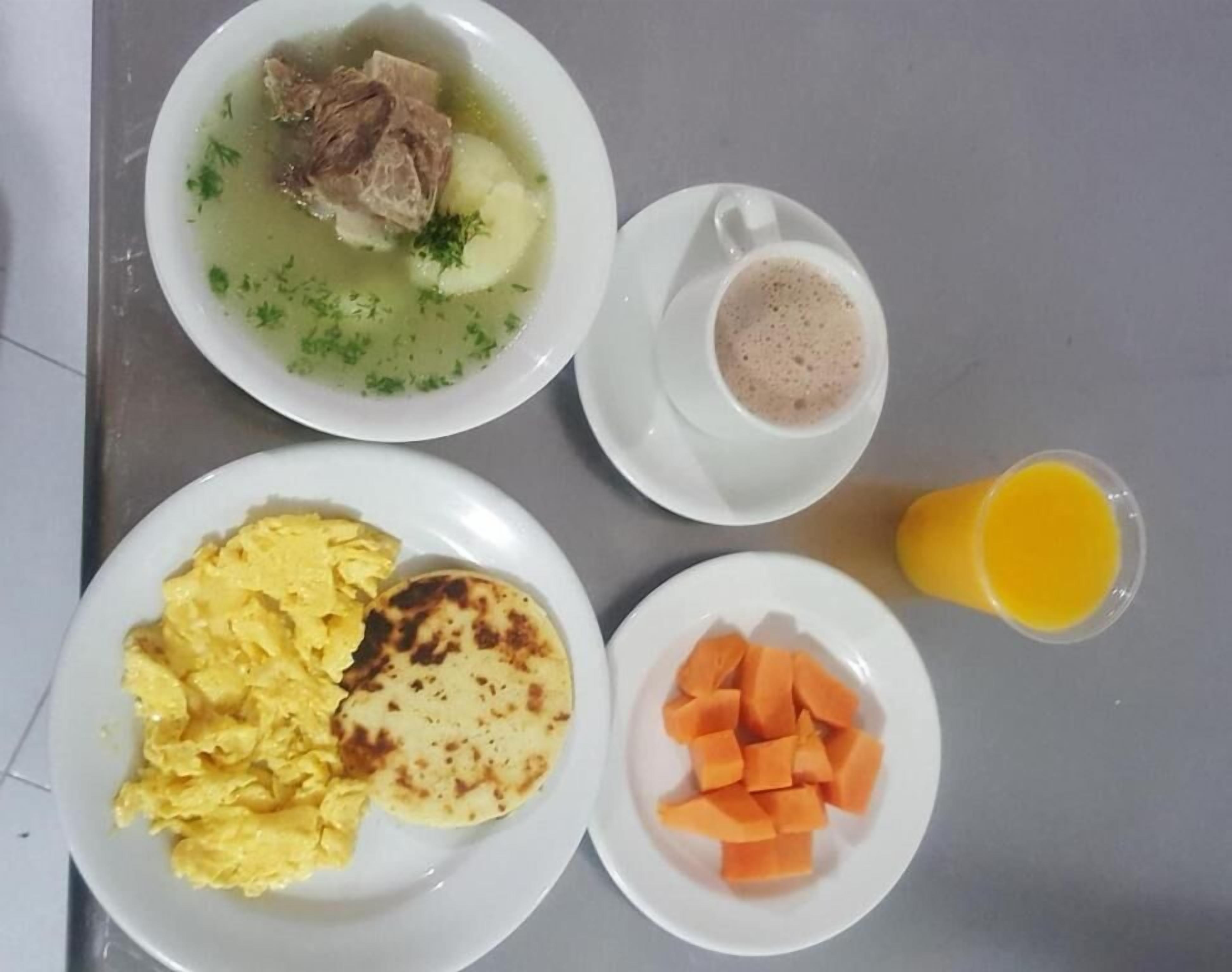 A breakfast setting with a bowl of soup, scrambled eggs, a plate of toast, a cup of coffee, and a glass of orange juice.