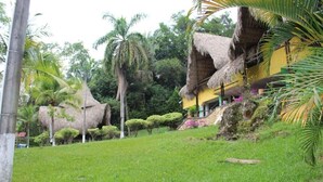 Resort tropical com edifícios de palha, vegetação exuberante e gramado bem cuidado.