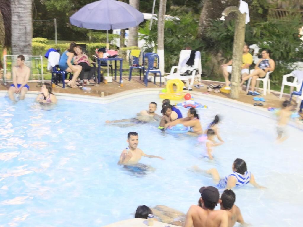 A swimming pool with people enjoying the water, surrounded by chairs and umbrellas.