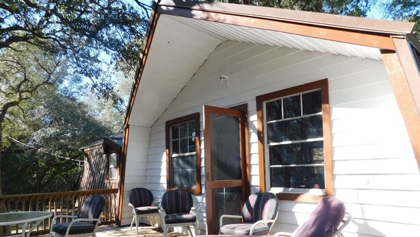 A covered porch with white railings, multiple windows, and outdoor furniture including chairs and a table.