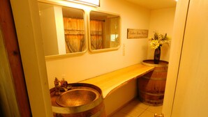 A bathroom with a wooden vanity, a sink, and two wooden barrels.