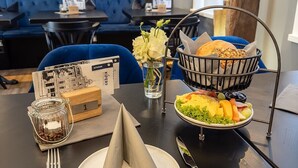 A dining table set with a plate of food, a basket of bread, a glass of water, a coffee jar, and a napkin cone. - Hotel Markt 5 (Lubbecke)