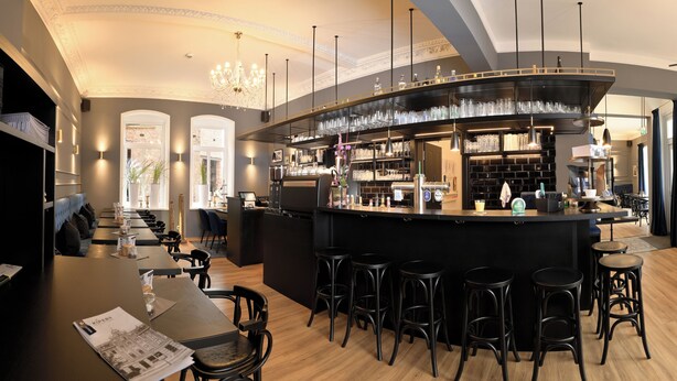 A modern bar area with a curved counter, multiple stools, and a seating area with tables and chairs. - Hotel Markt 5 (Lubbecke)