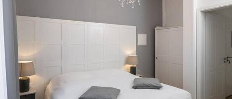 A bedroom with a large bed, two bedside lamps, a chandelier, and a wardrobe.