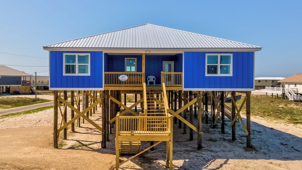Una casa azul con techo de metal, terraza de madera y una escalera que lleva a la entrada.