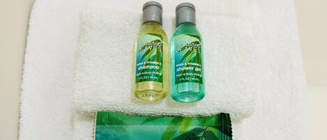 A white towel with two bottles of 'rainkissed LEAVES' bath and body wash and shower gel, and a packet of 'MOISTURIZING bath soap' on a bathroom counter.