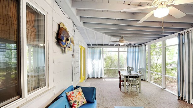 Un patio techado con un sofá azul, una mesa de comedor con sillas y un ventilador de techo.