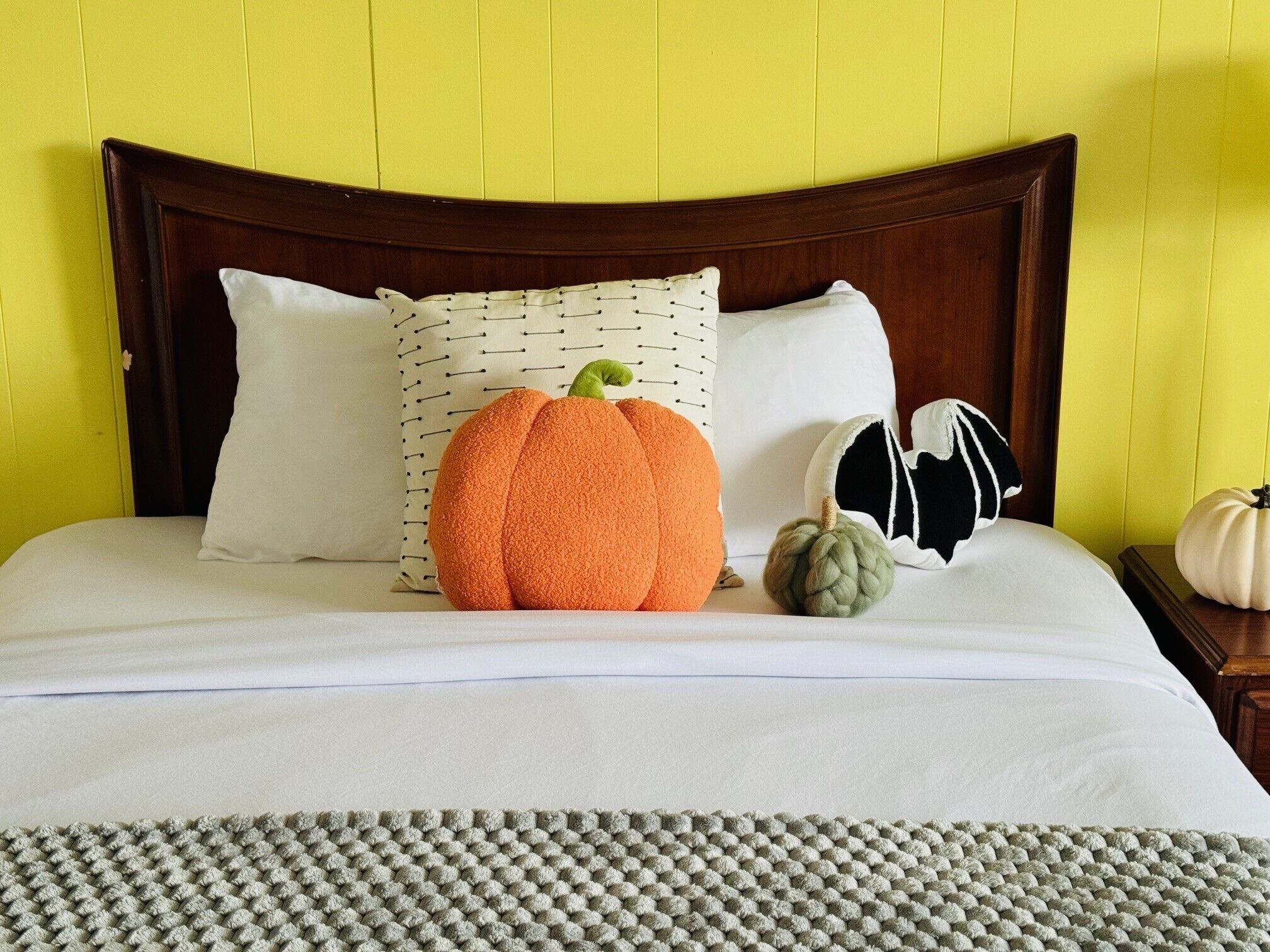 A bed with a wooden headboard, white pillows, and a large orange pumpkin-shaped pillow.