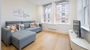 A modern living room with a grey sectional sofa, a flat-screen TV, and artwork on the wall. - Orient Residence Manchester (Manchester)
