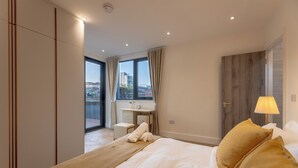 A modern hotel room with a large bed, a desk, and a view of the city through the windows. - Orient Residence Manchester (Manchester)