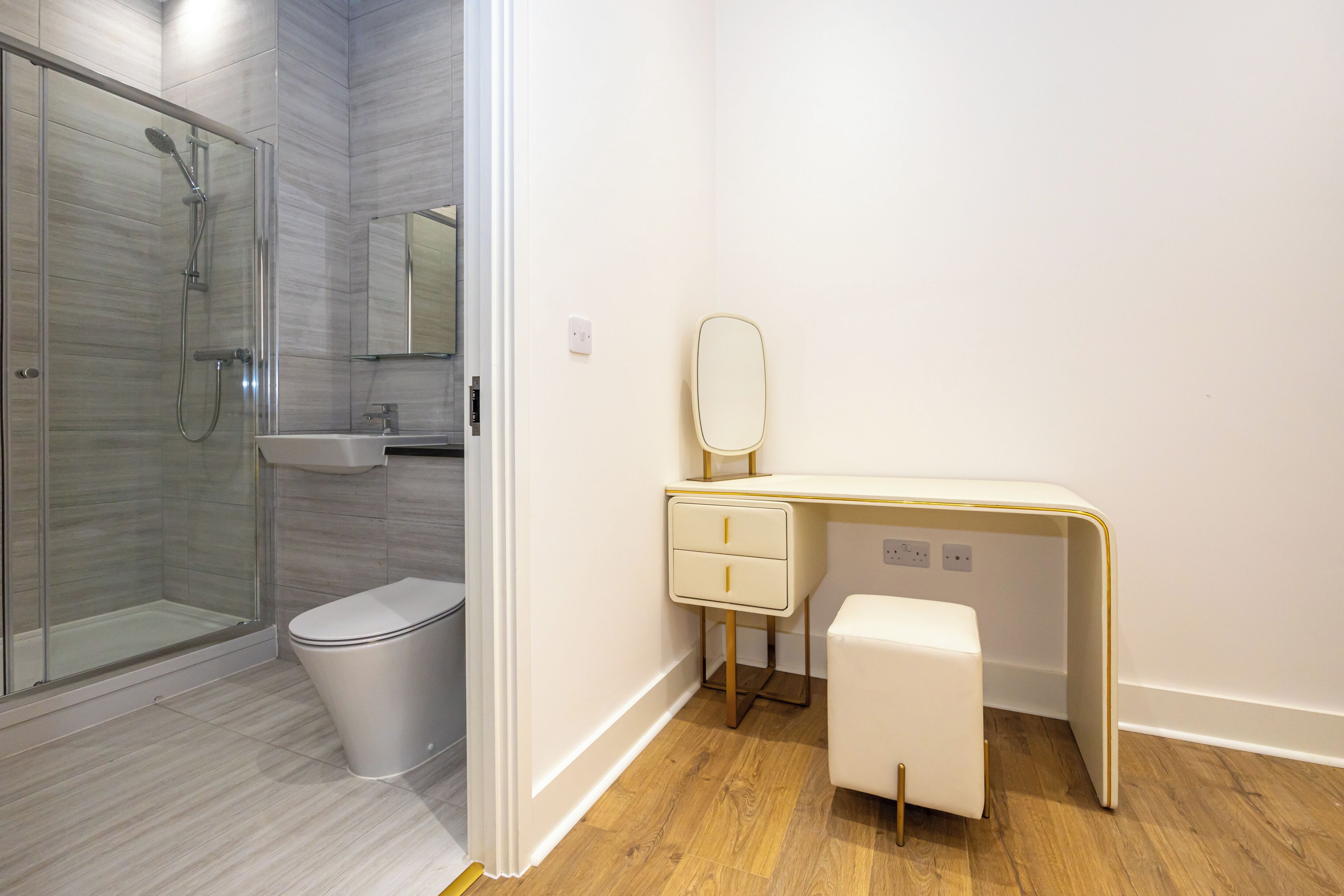 A modern bathroom with a glass shower enclosure, a toilet, a vanity with a mirror, and a small stool.