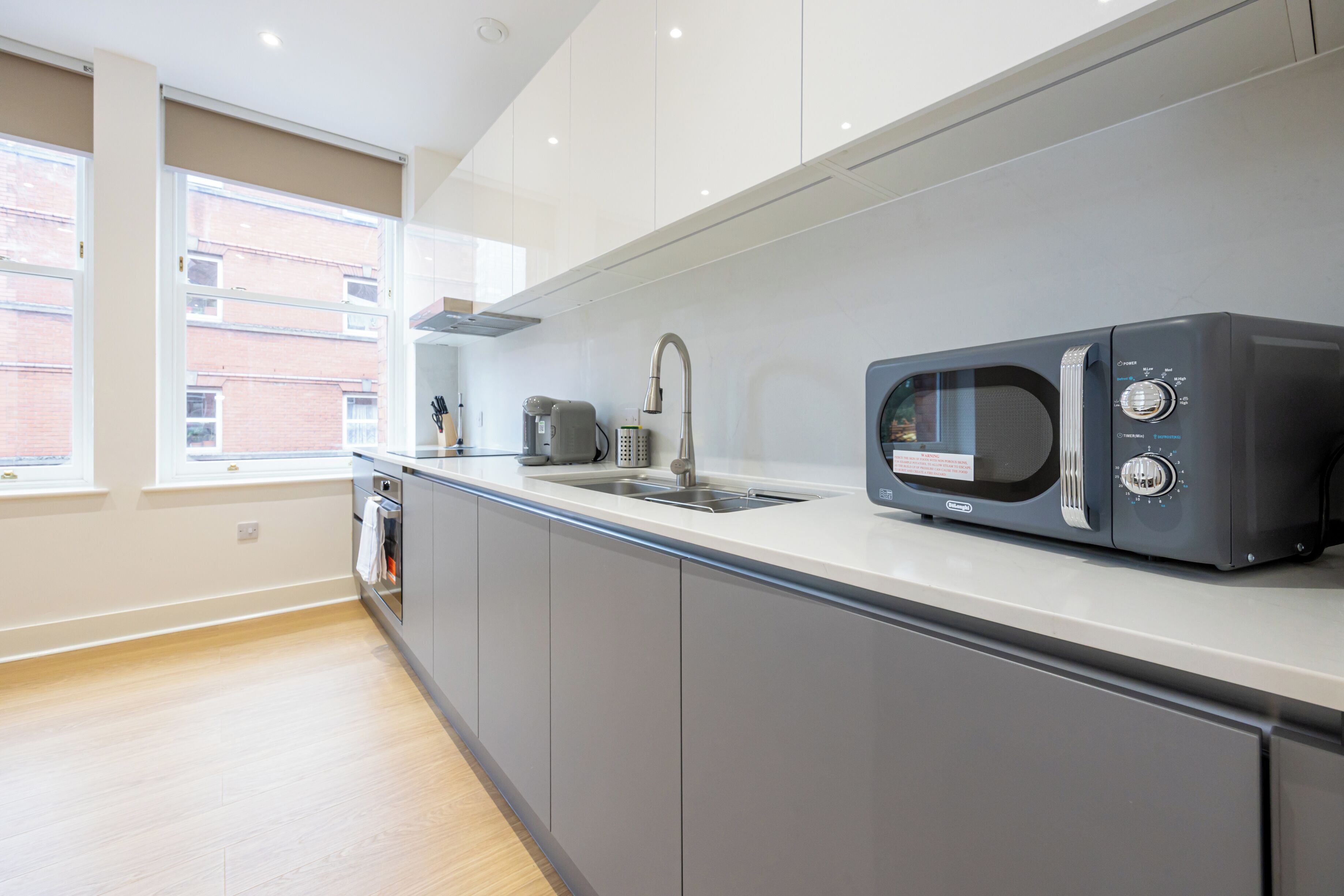 A modern kitchen with grey cabinets, a built-in microwave, and a window providing natural light.