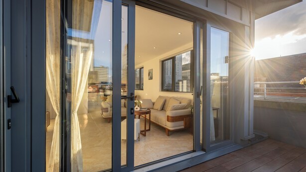 A modern living room with a sofa and coffee table, large sliding glass doors leading to an outdoor deck. - Orient Residence Manchester (Manchester)