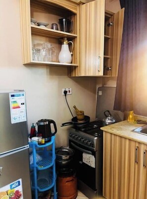 Une cuisine compacte avec des meubles en bois, une cuisinière à gaz, une bouilloire et un distributeur d’eau bleu.